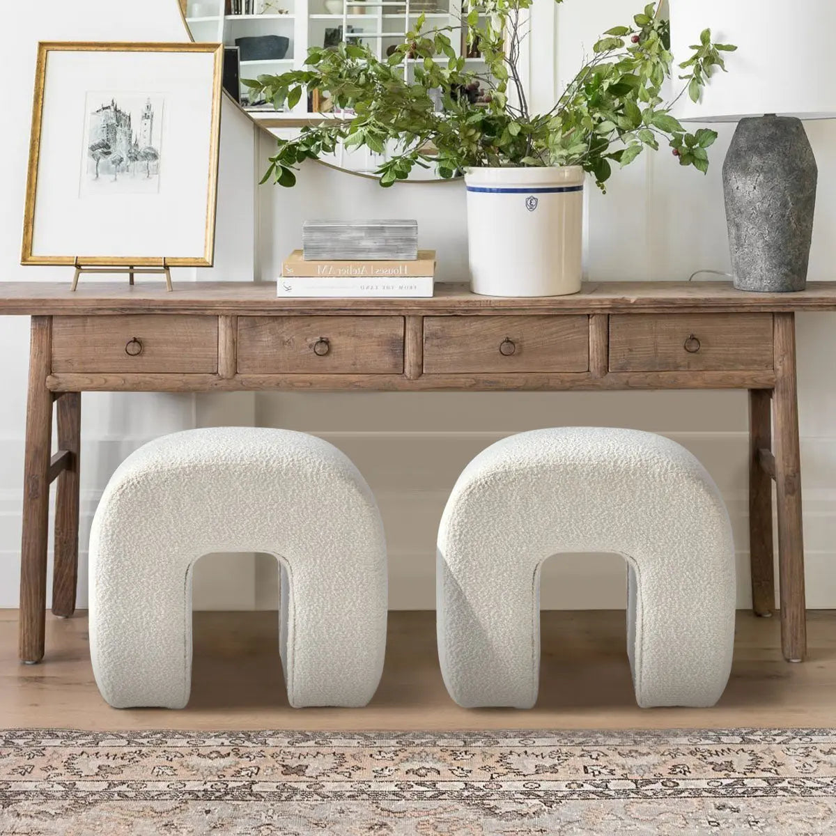 Pair of Lily Beige Boucle Ottomans under wooden console, beige rug, white walls, living room.