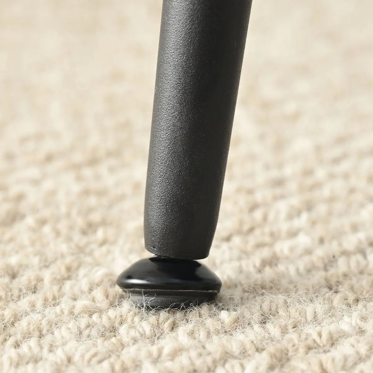 Close-up of Lucca Black Rattan Boucle Dining Chair leg on beige carpet in living room.