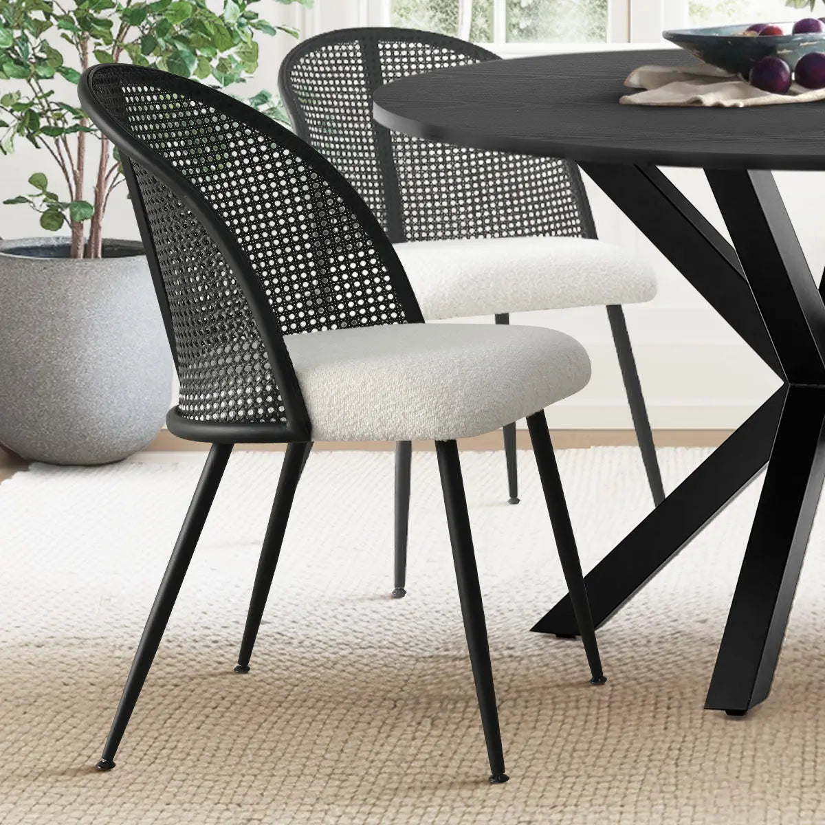 Lucca Black Rattan Boucle Dining Chair, natural rug, modern dining table, and decorative plant in room.