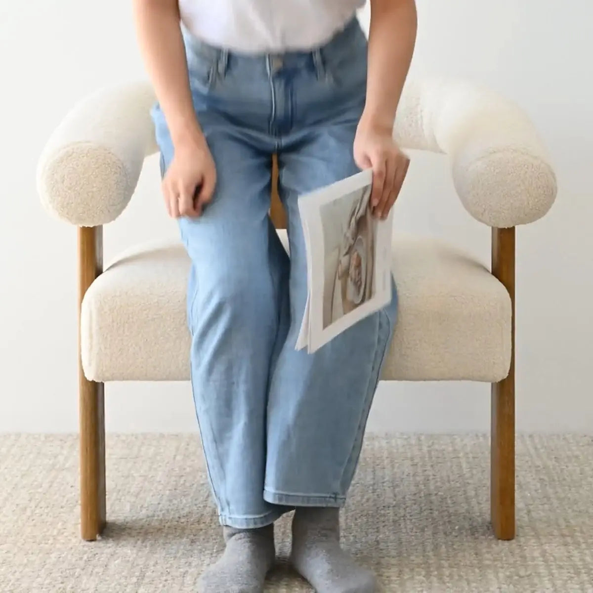 Maye Beige Boucle chair with arms in living room, neutral carpet, woman holding magazine.