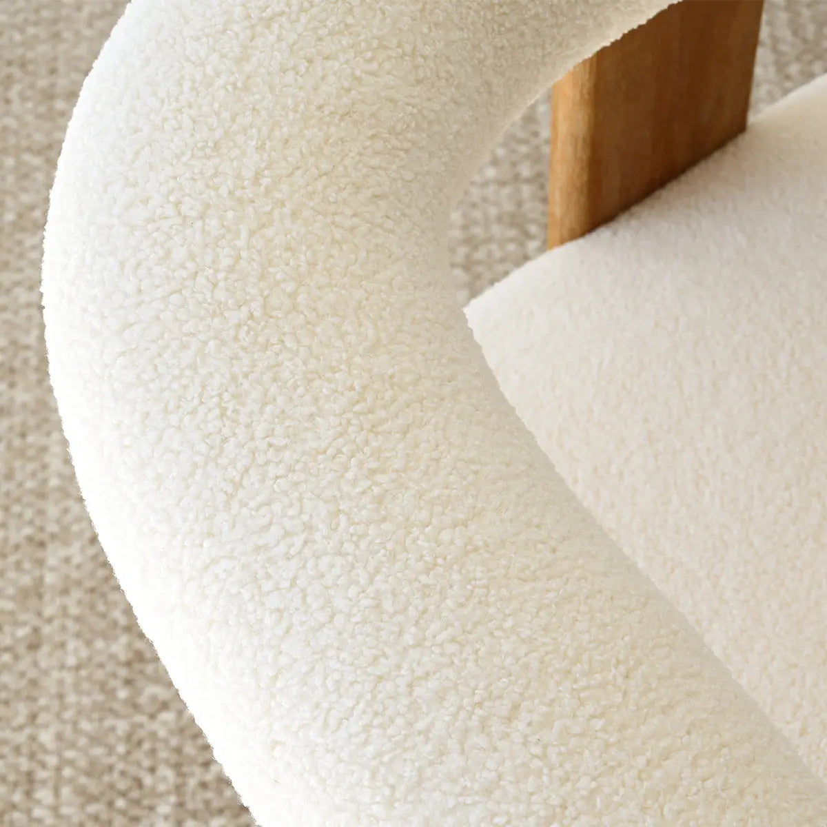 Close-up of Maye Beige Boucle Chair texture on beige carpet flooring, featuring wooden armrest detail.