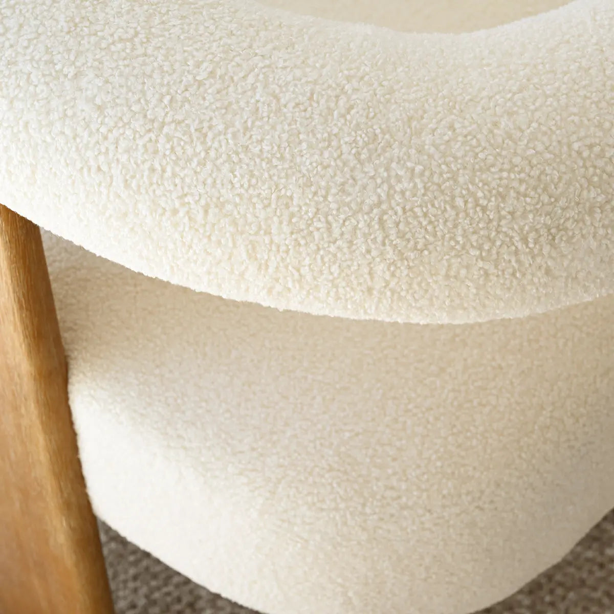 Close-up of Maye Beige Boucle upholstered chair fabric texture, wooden arm detail in living room.