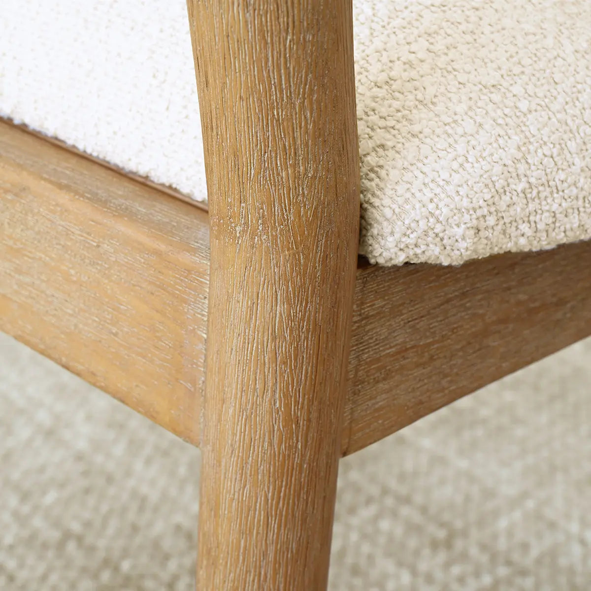 Close-up of Maye Boucle Beige Upholstered Dining Chair's wooden frame on textured carpet.