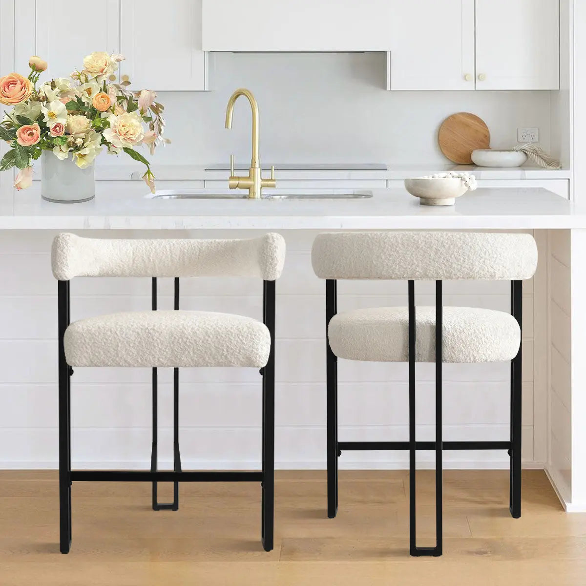 Mia beige upholstered counter stools with arms, white kitchen, wood flooring, gold faucet, floral decor.