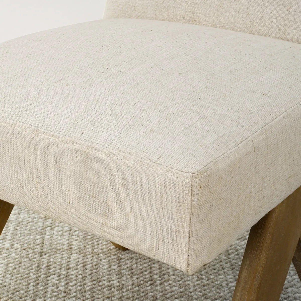 Close-up of Morgan Mid-Century Boucle Upholstered Dining Chair fabric and wood legs on textured carpet.