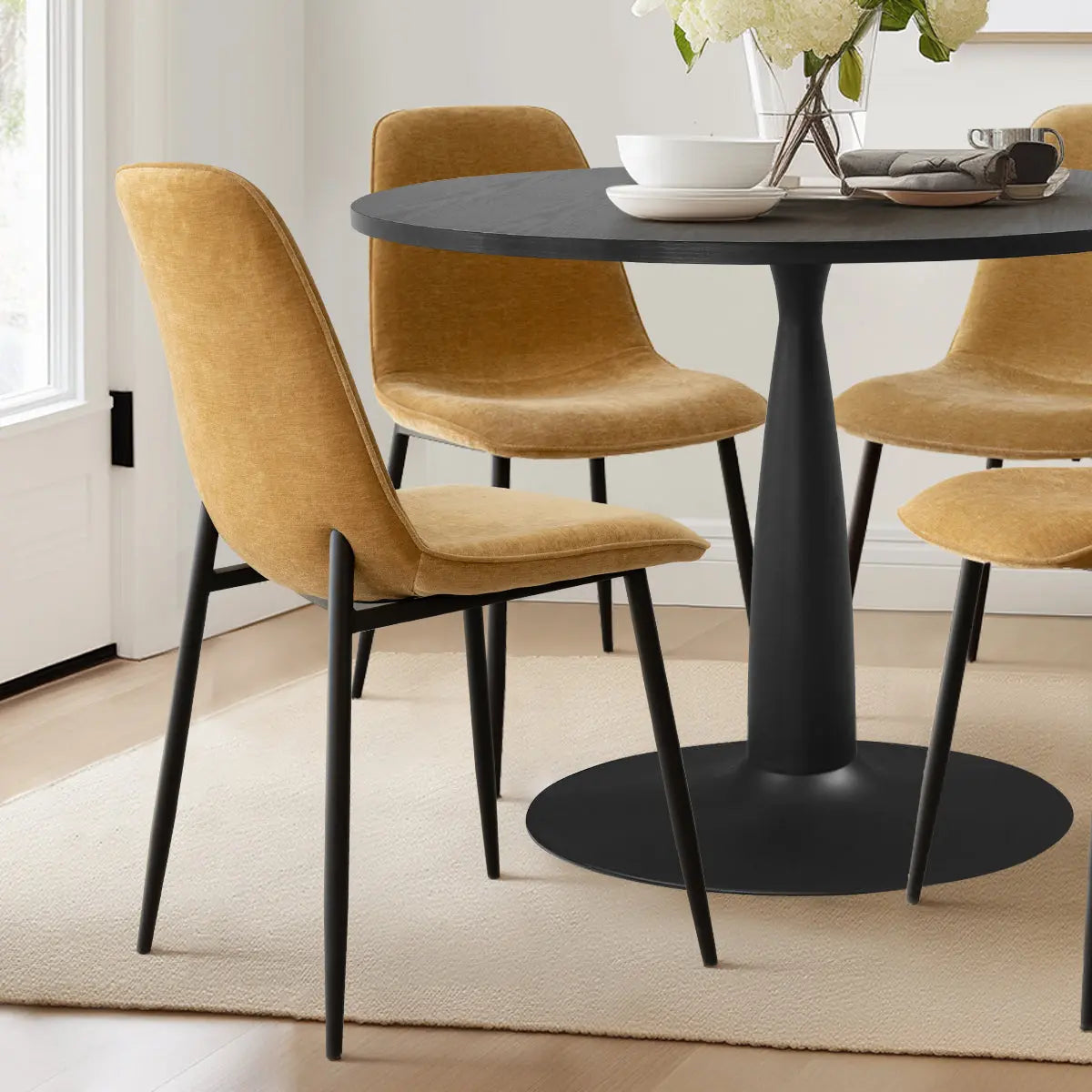 Haven & Oslo dining set with black round table, mustard chairs, in modern dining room, light flooring.