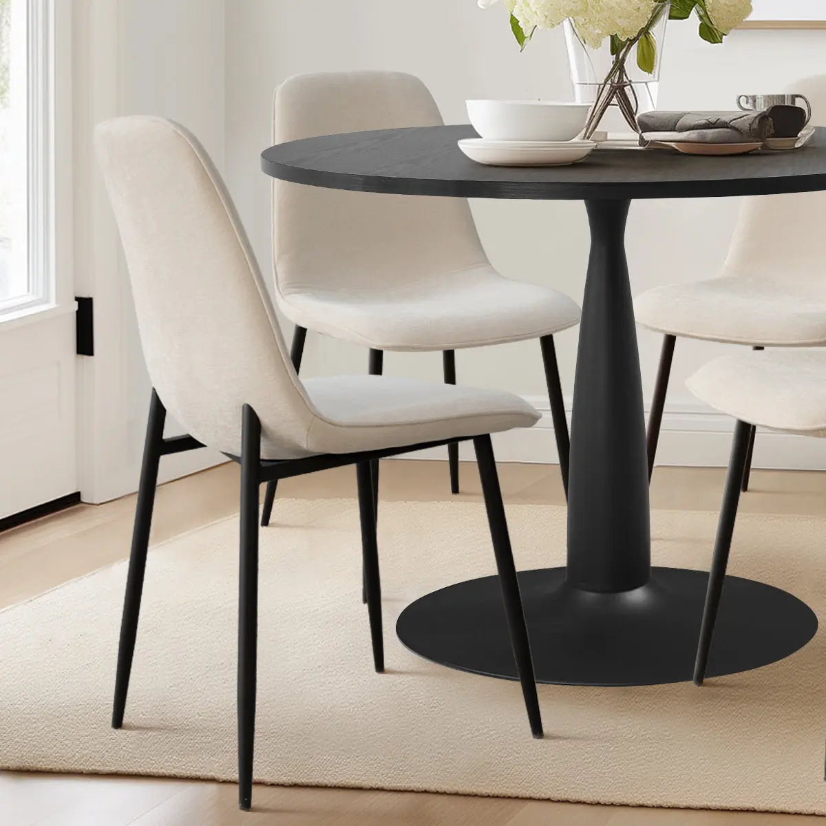 Haven & Oslo black dining set with beige chairs, white wall, light wood flooring, in dining room.