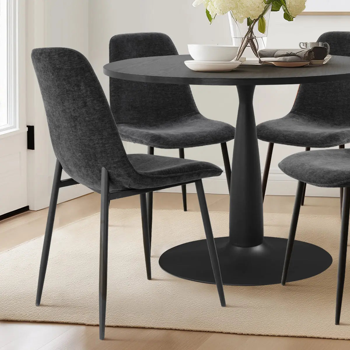 Haven & Oslo black round table set with gray chairs, hardwood floor, in modern dining room.