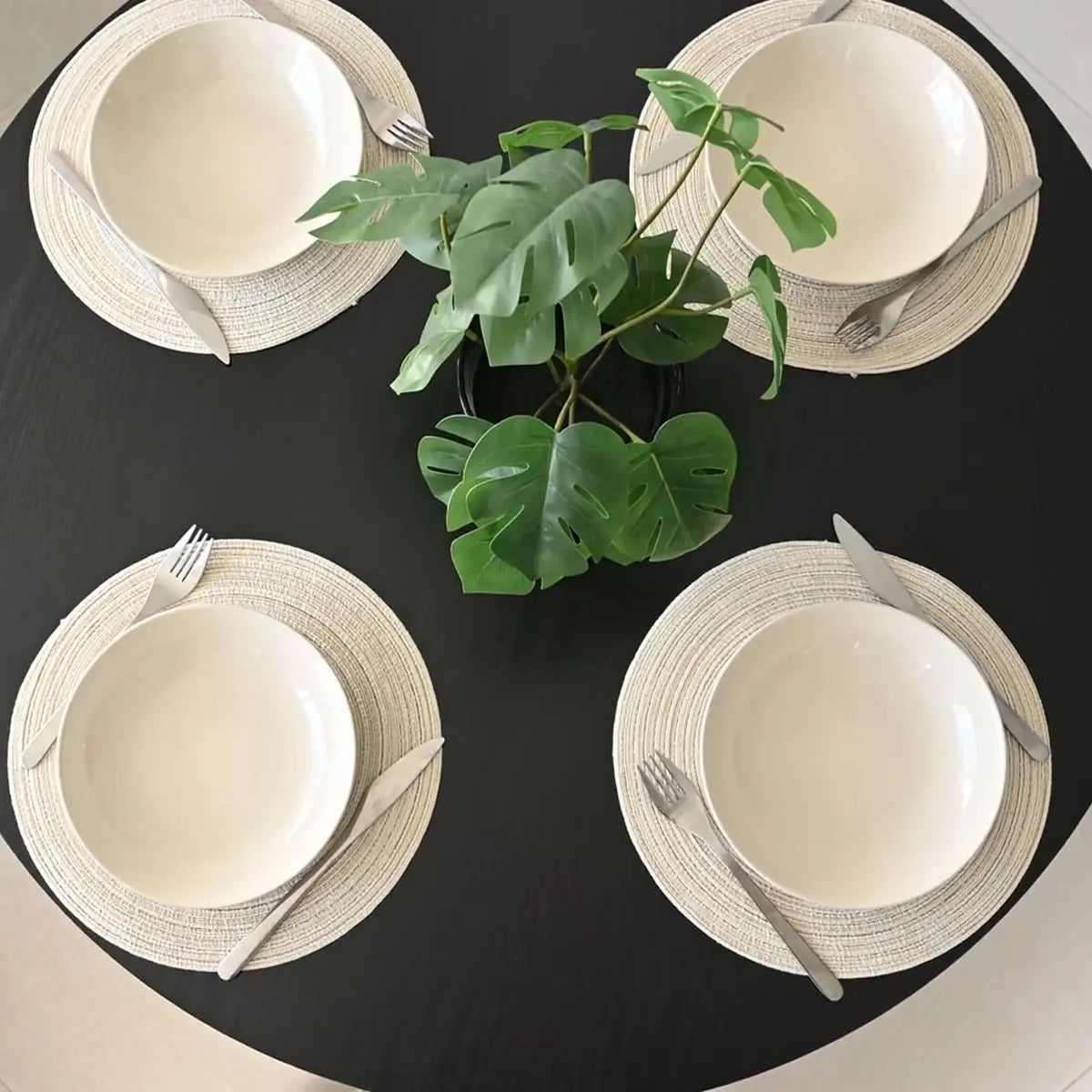 Haven round dining table with white place settings, black surface, and green leaves centerpiece.