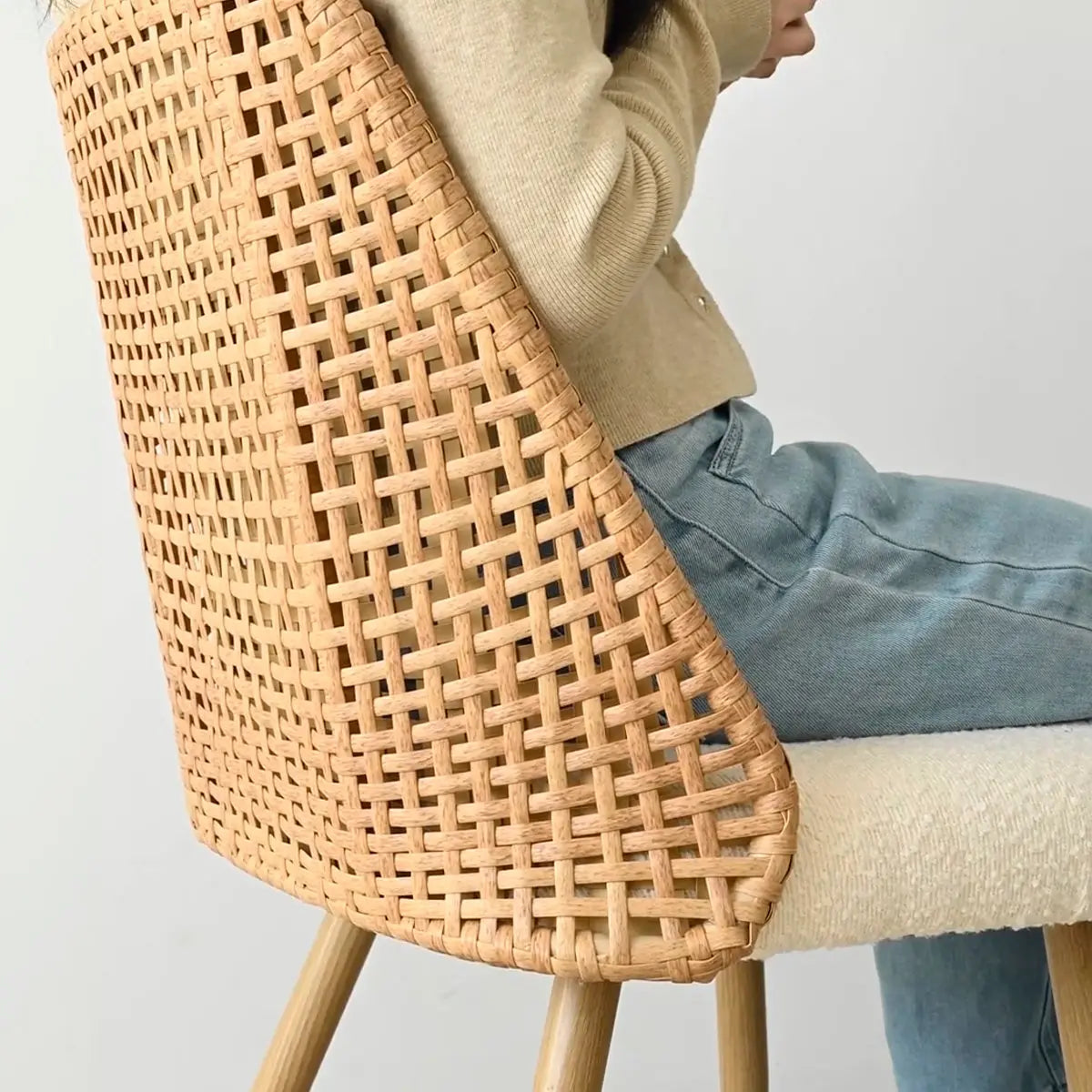 Close-up of Dwen & Nice rattan chair with beige cushion and jeans, in dining setting.