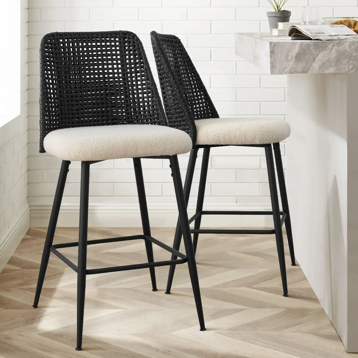 Black rattan counter stools with white brick wall, chevron wood flooring in modern kitchen setting.