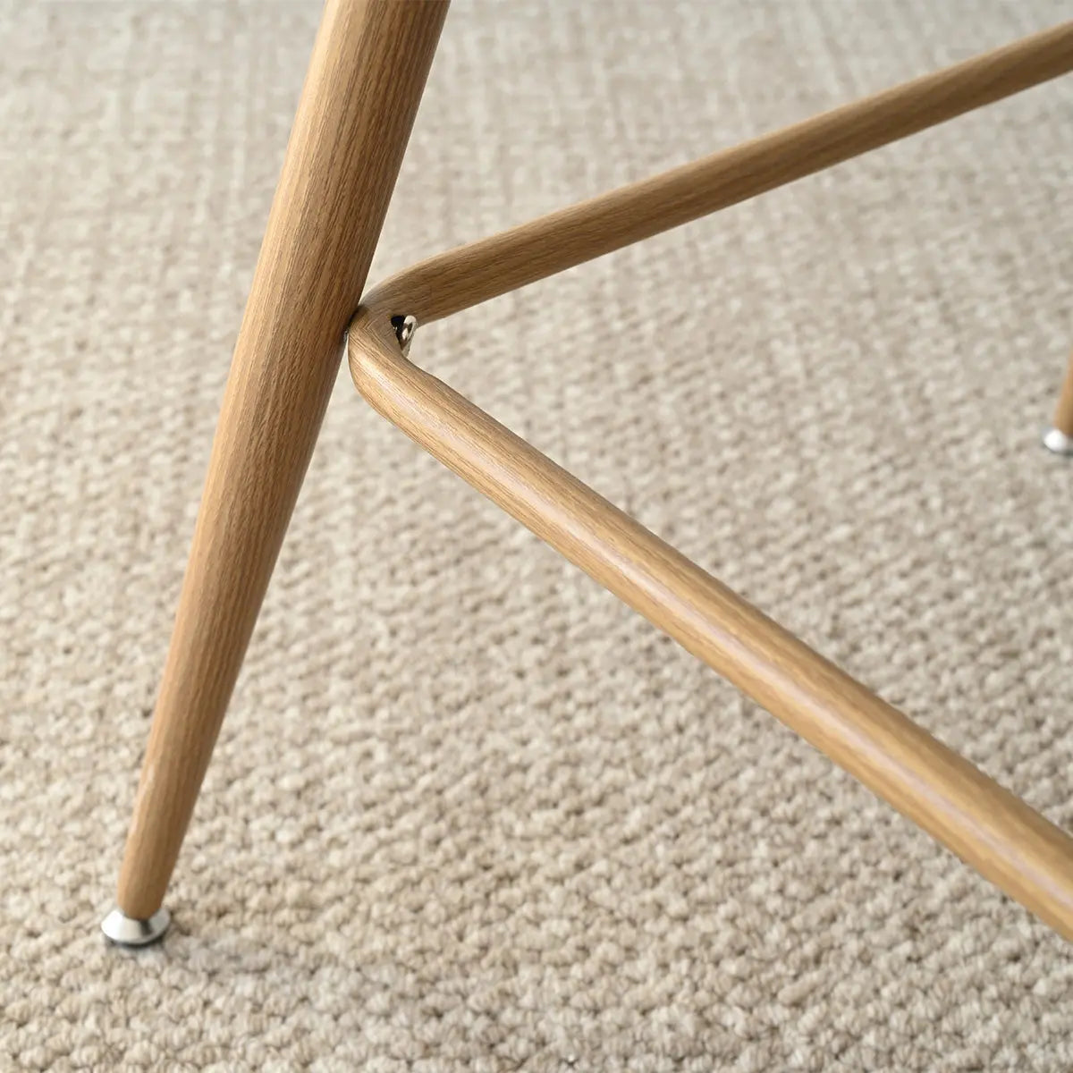 Leg detail of Nice Modern Rattan Upholstered Counter Stool on beige carpeted floor.