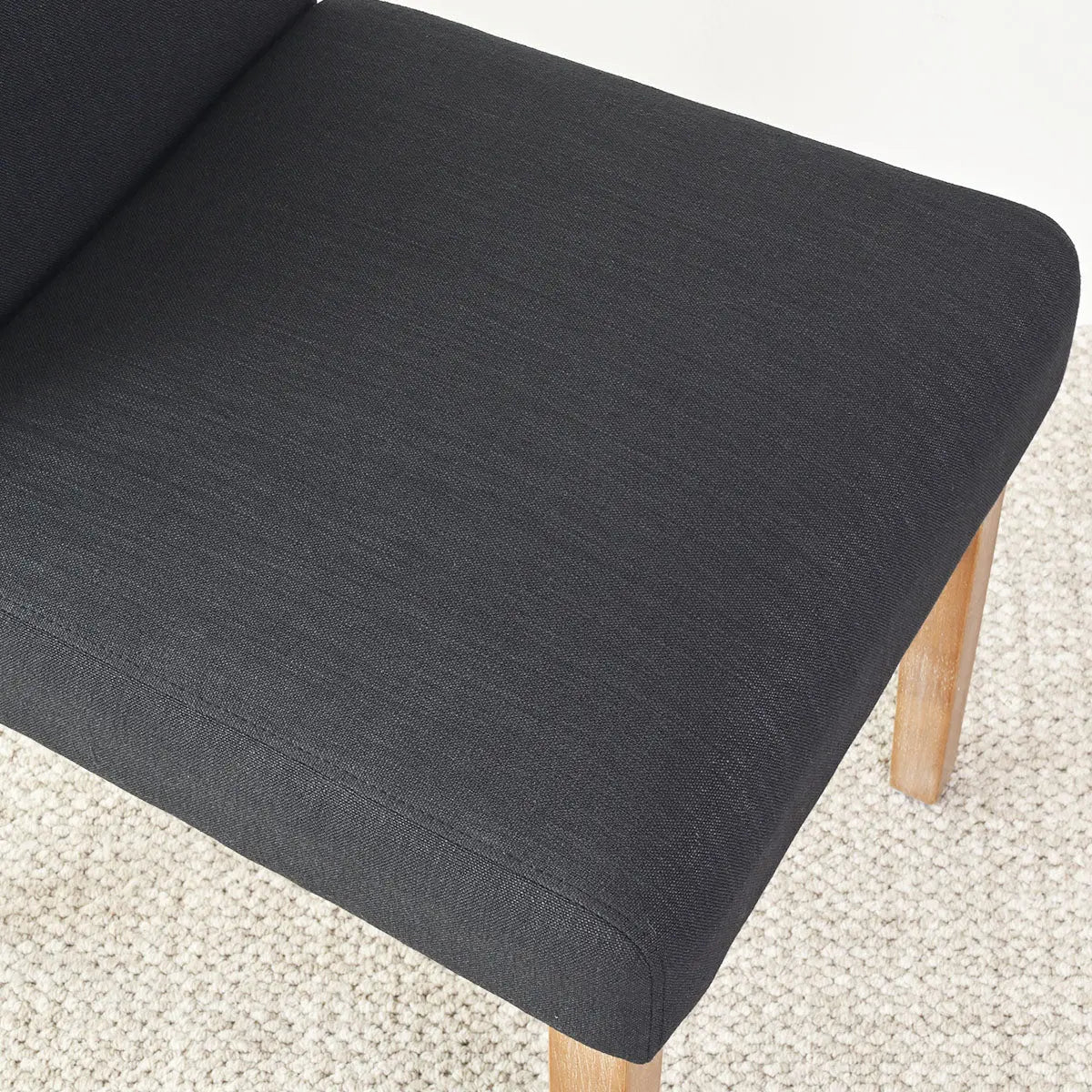 Dark gray upholstery of North Chair with light wood legs on a textured carpet flooring.