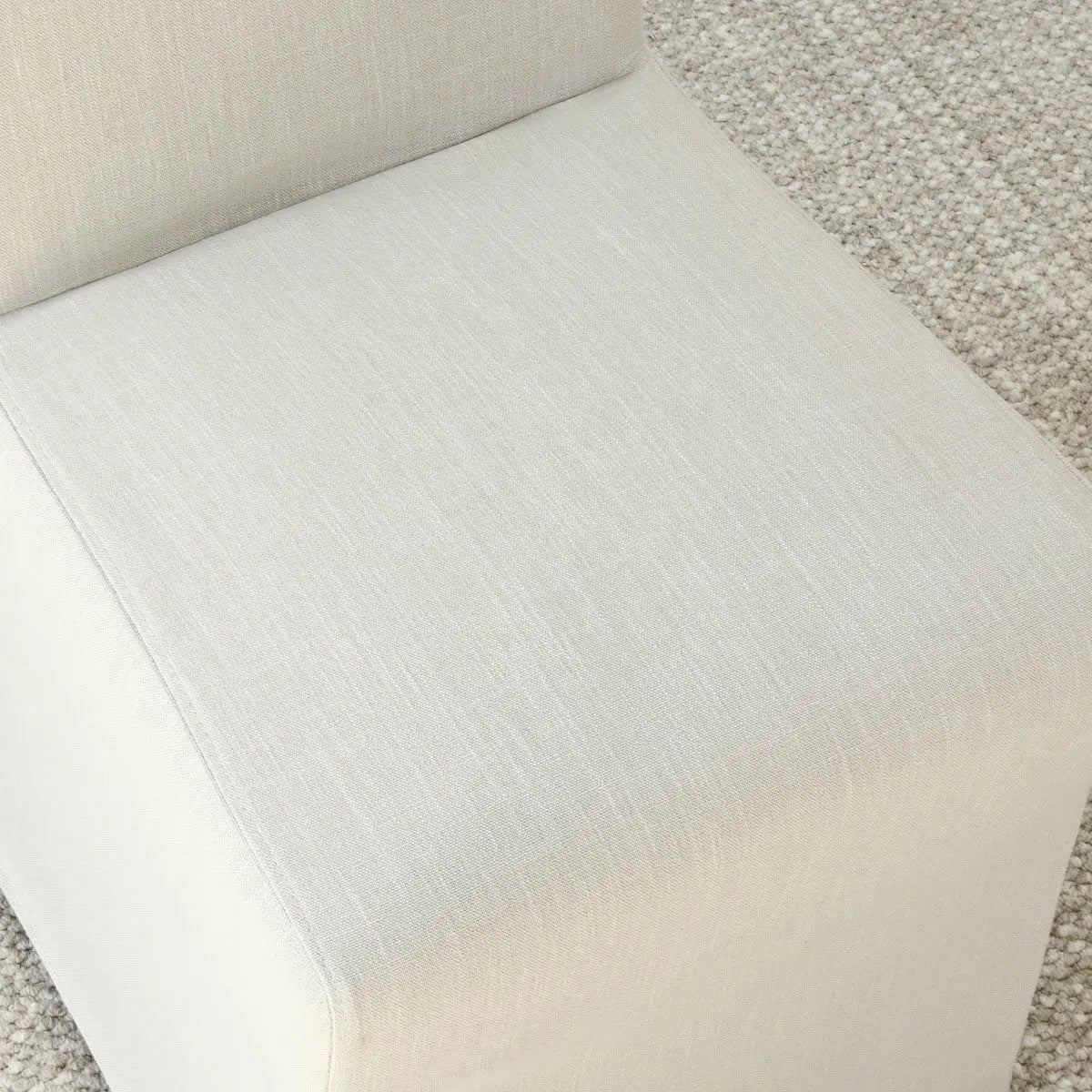 Close-up of North Beige Upholstered Dining Chair with Removable Slipcovers against textured carpet flooring.