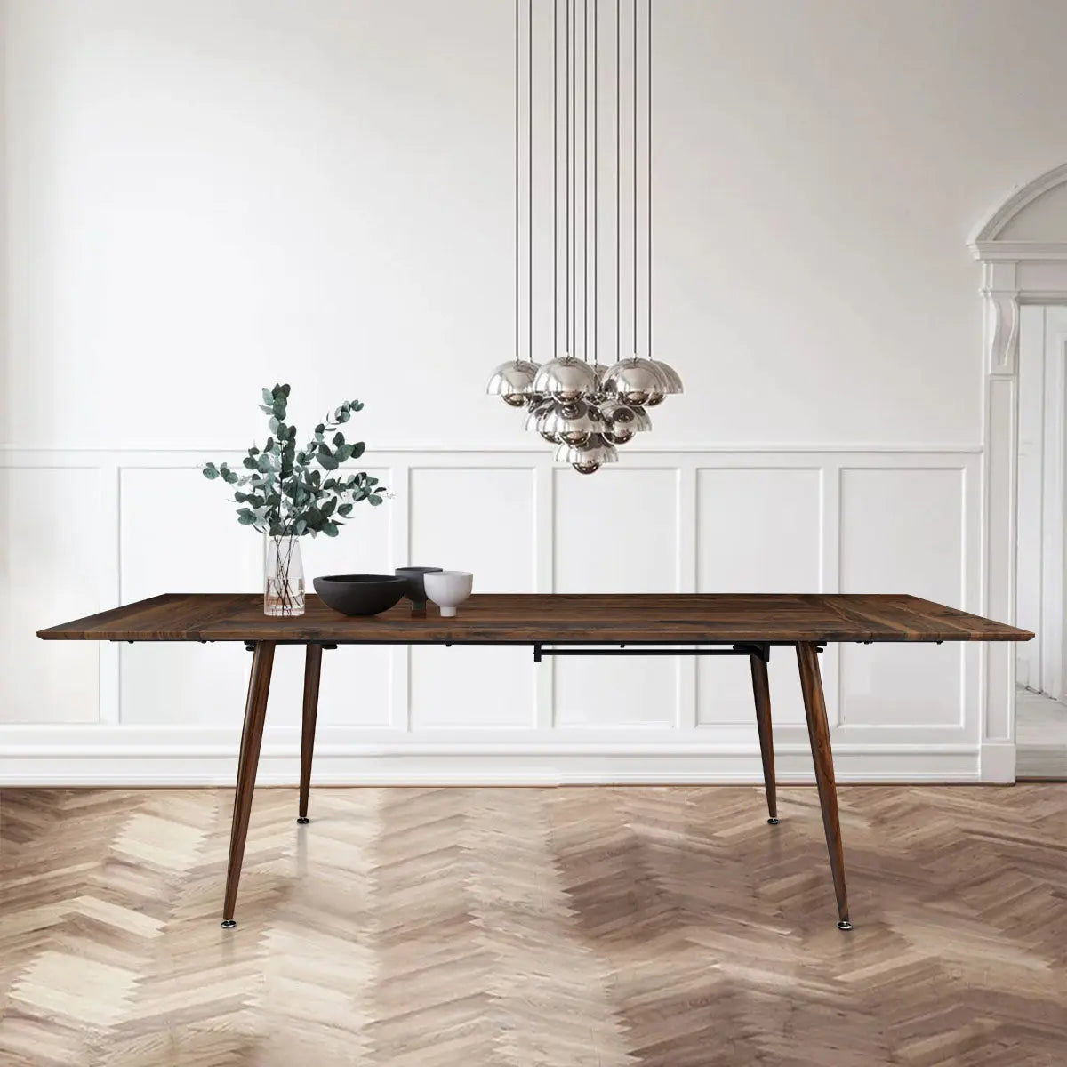 Odense Extendable Dining Table with modern chandelier, herringbone flooring, and white paneled walls.