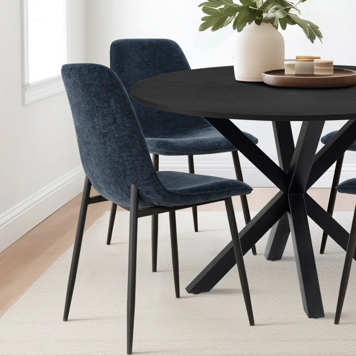 Oliver & Oslo dining table set with navy chairs, light rug, white wall in dining room.