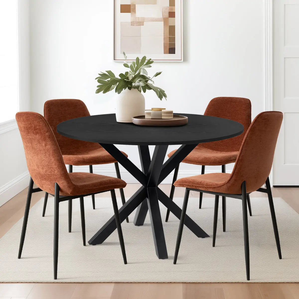 Oliver & Oslo Round Dining Table Set with orange chairs, white walls, light hardwood flooring, artwork.