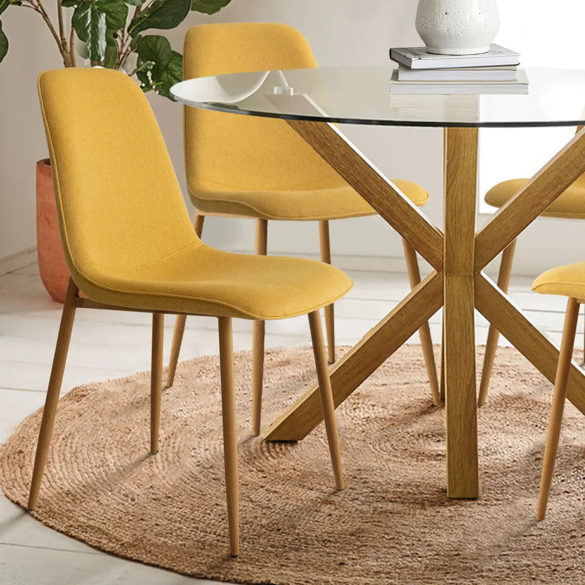 Oliver & Oslo glass round dining table set, yellow chairs, wooden legs, beige rug, hardwood floor.