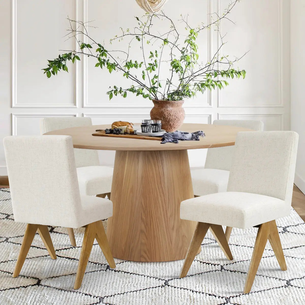 Orchid & Morgan Solid Oak Round Dining Table Set with white chairs, textured rug, and paneled walls.