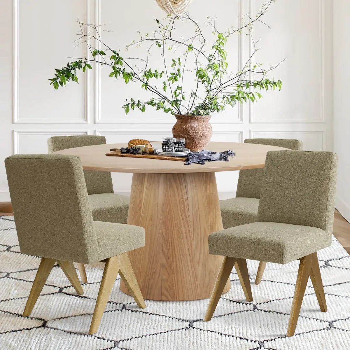 Orchid & Morgan Solid Oak Round Dining Table Set with green chairs, white paneled walls, patterned rug.