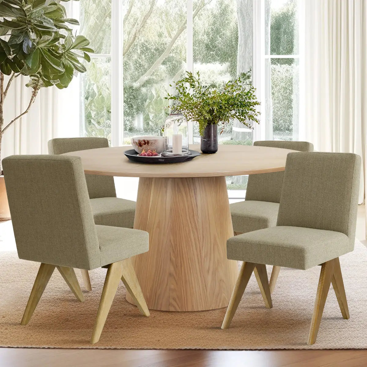 Orchid & Morgan oak round dining table set in living room with green chairs, beige rug, window view.