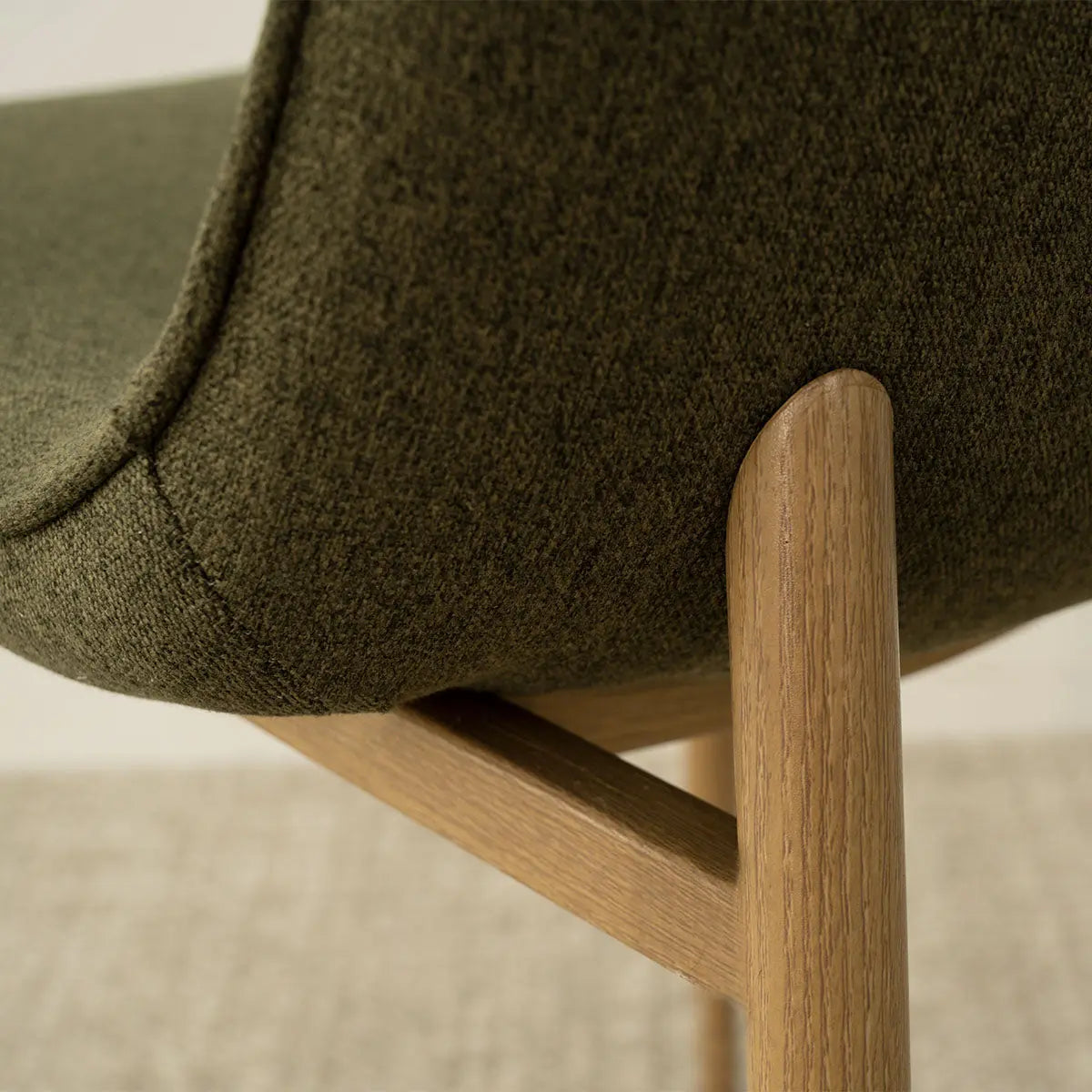 Close-up of Oslo Chenille Dining Chair's oak legs and textured upholstery on light carpet.