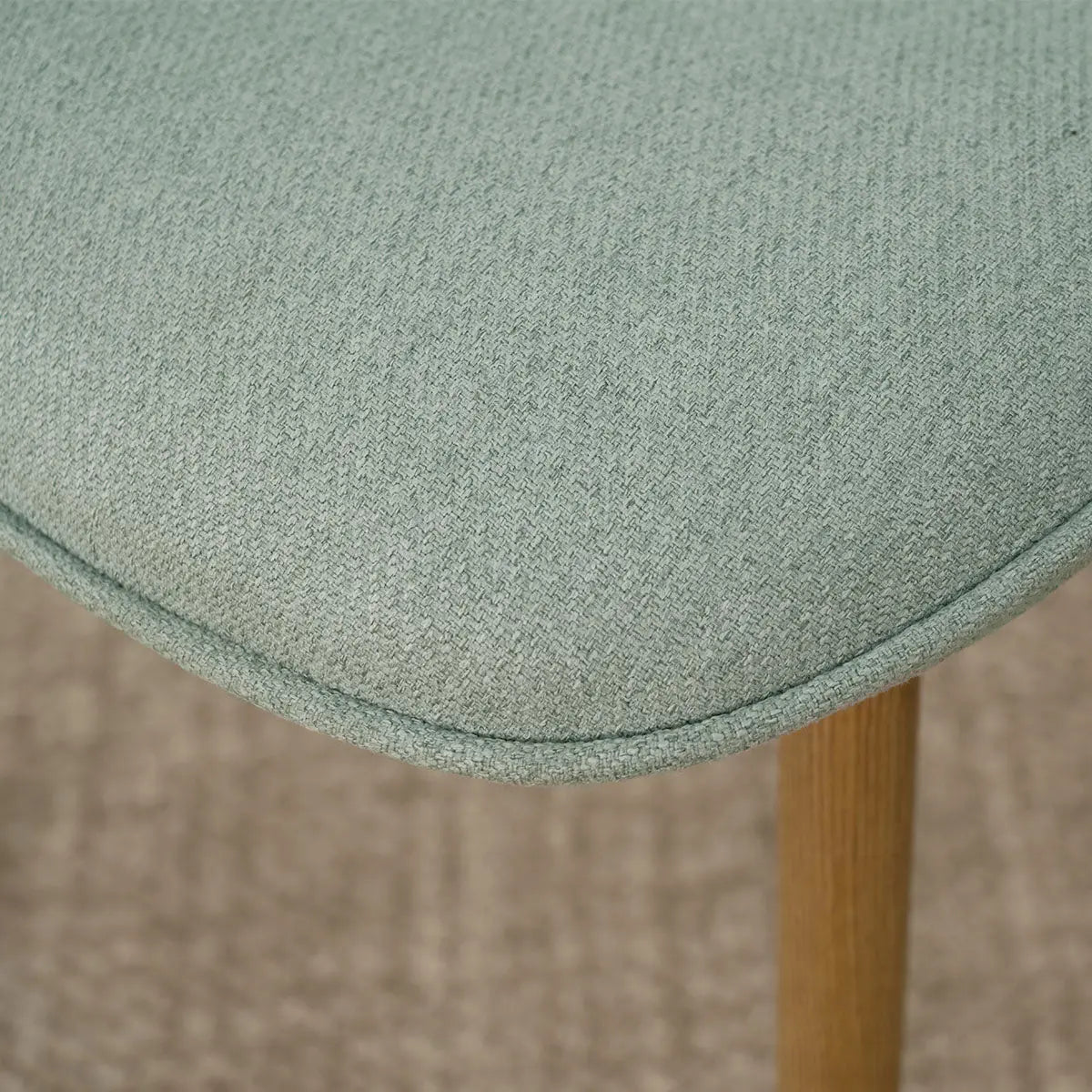 Close-up of Oslo Chenille Dining Chair seat, oak legs, textured upholstery detail, beige flooring.