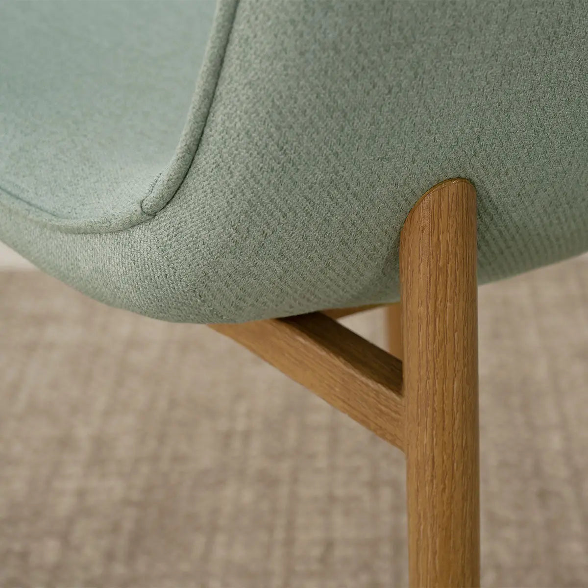 Close-up of Oslo Chenille Dining Chair with oak legs on textured beige carpet. Scandinavian style.