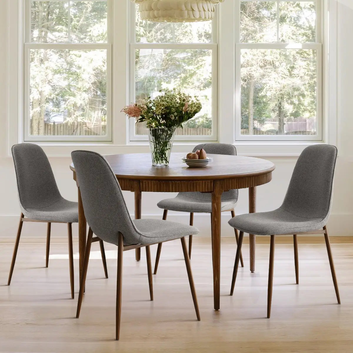 Oslo dining chair with walnut legs and round table in bright dining room, light wood flooring.