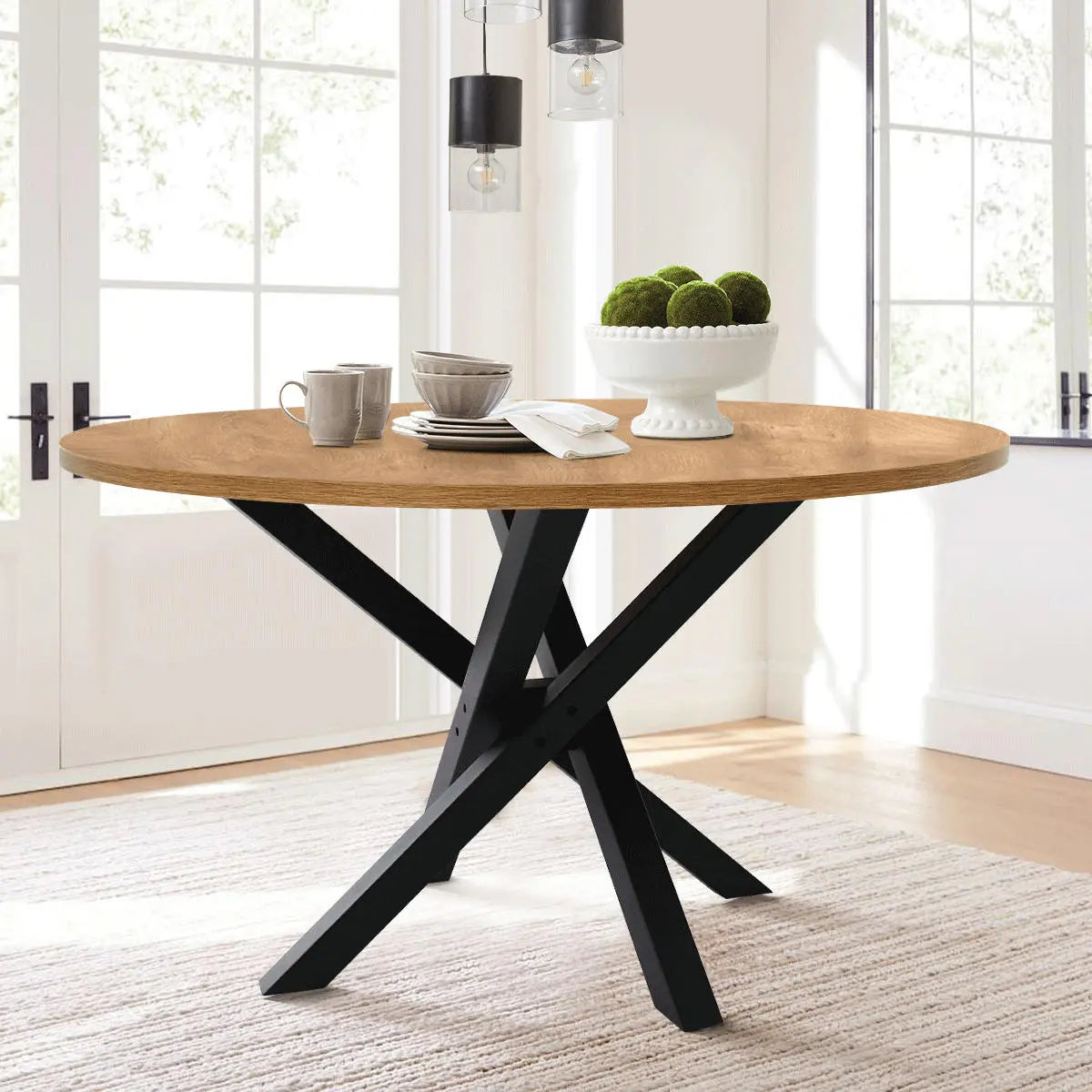 Robert Modern Round Dining Table with black legs in bright dining room, wood flooring, and pendant lights.