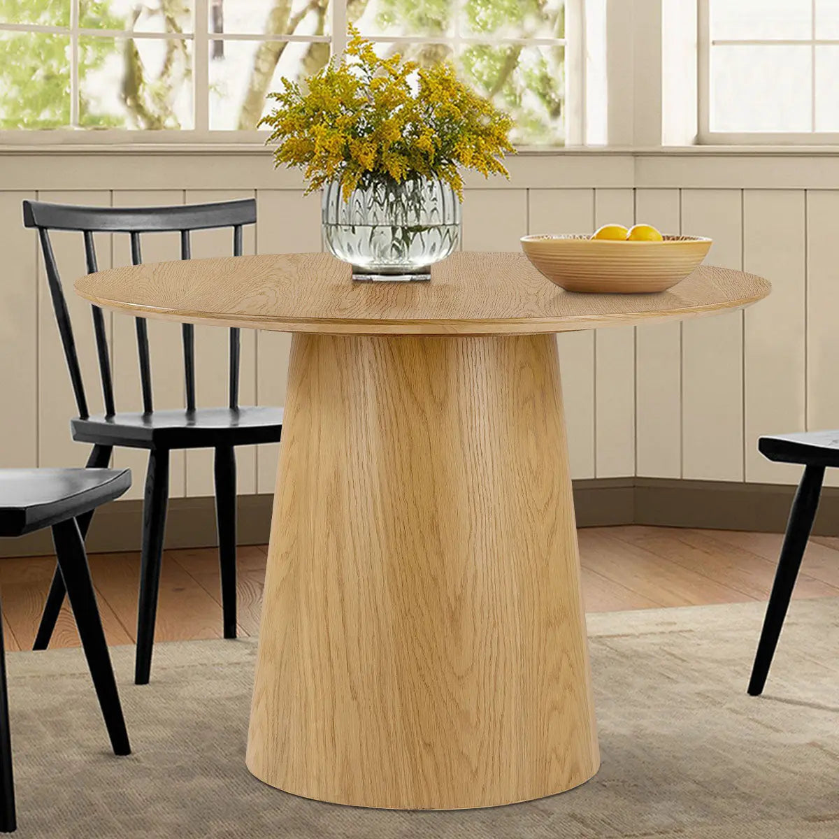 Saigong Oak Round Dining Table in cozy dining room, black chairs, wooden floor, paneled walls.