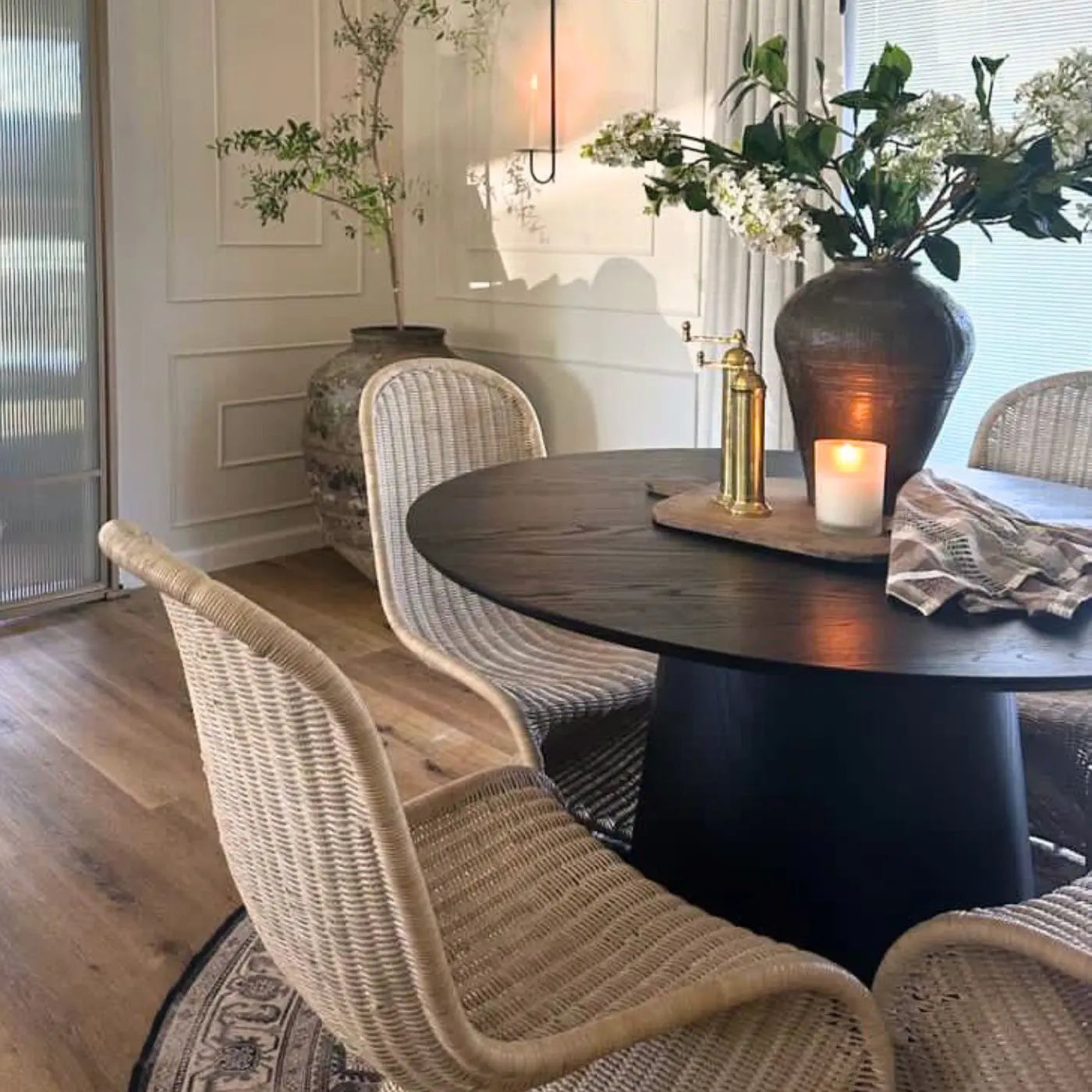 Dining room with Saigong Oak Round Dining Table, wicker chairs, wooden flooring, light wall paneling.