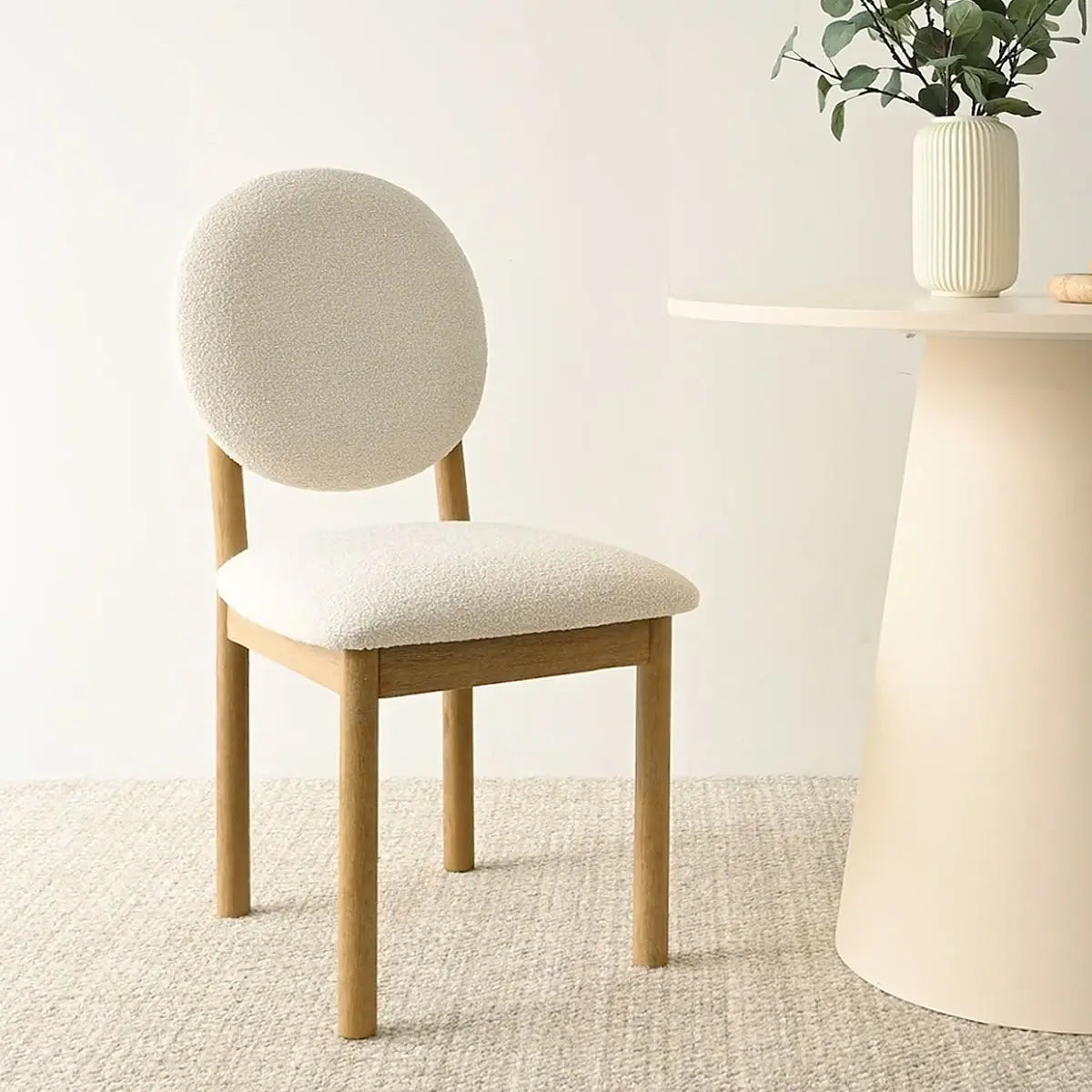 Maye Boucle Beige Upholstered Dining Chair beside minimalist table, cream walls, textured carpet flooring.