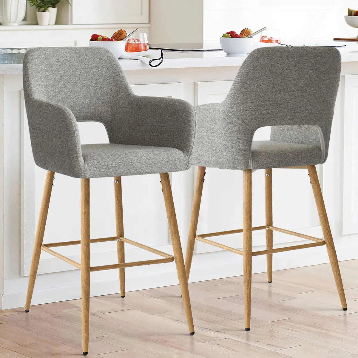 Atlanta Modern Upholstered Counter Stool with Arms in kitchen; gray upholstery, wooden legs, light flooring.