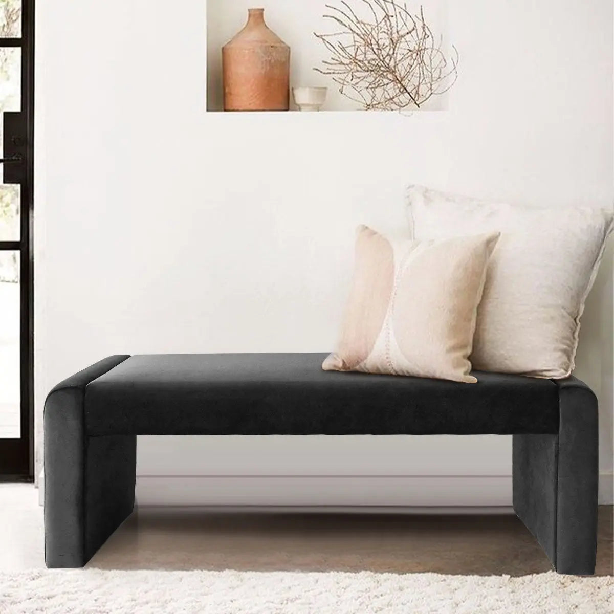 Black leather and velvet bench with minimalist cushions, white walls, beige carpet in living room.