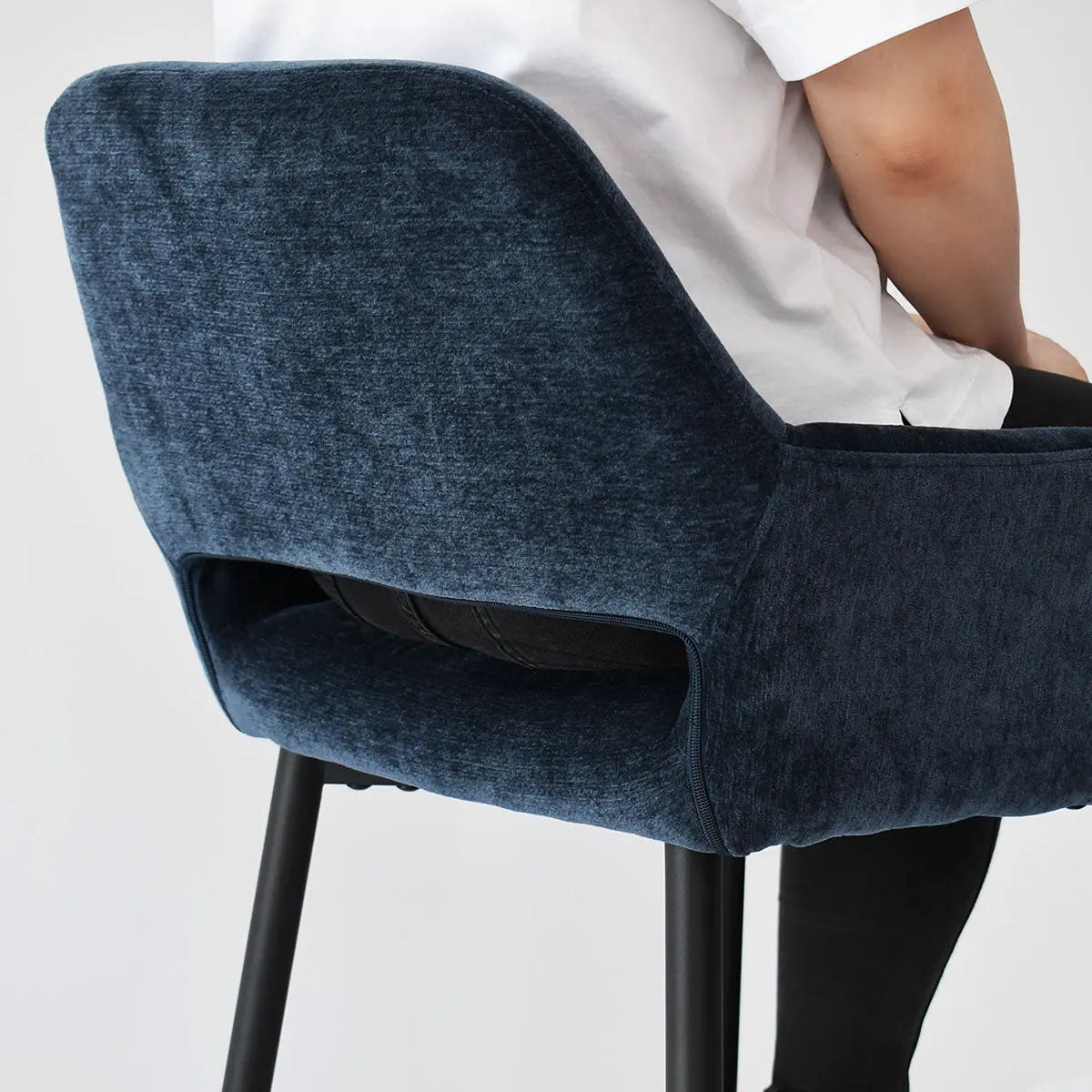 Modern navy upholstered counter stool with arms, seated person visible, solid background.